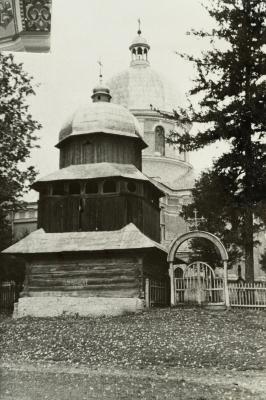 Wooden Bell Tower Next to a Stone Church — unknown